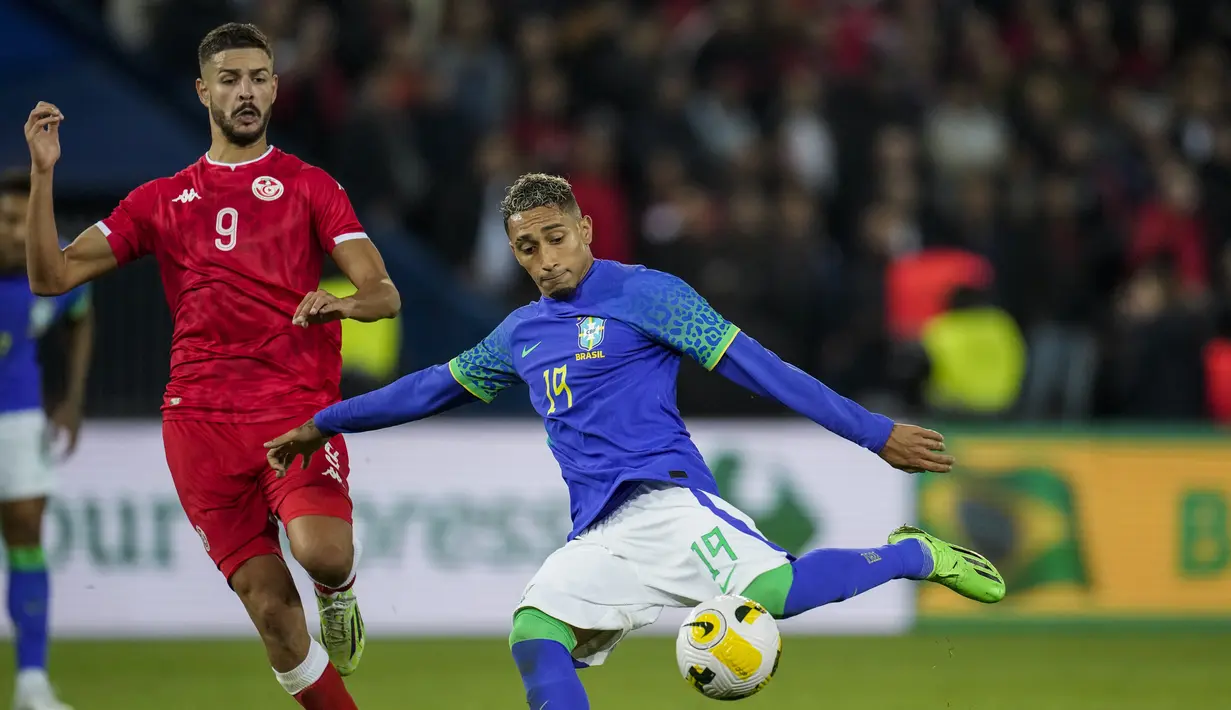 Penyerang timnas Brasil Raphinha menendang bola di sebelah gelandang Tunisia Mortadha Ben Ouanes dalam laga uji coba internasional kontra Brasil di Stadion Parc des Princes, Rabu (28/9/2022) dini hari WIB. Timnas Brasil menang dengan skor telak 5-1 atas Tunisia dalam pertandingan FIFA Matchday. (AP Photo/Christophe Ena)
