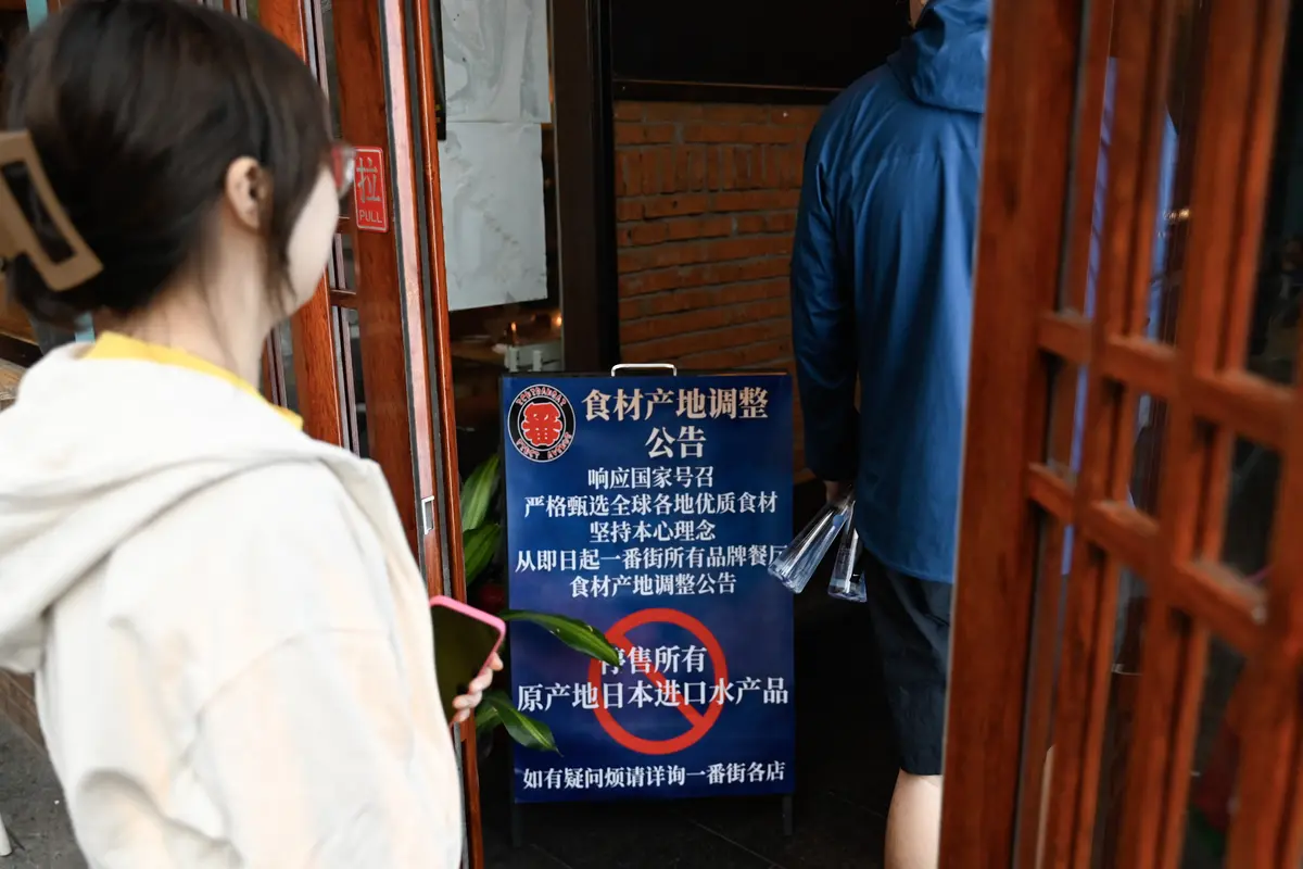 Orang-orang berjalan ke area restoran Jepang melewati papan bertuliskan "Tangguhkan penjualan semua produk ikan yang diimpor dari Jepang", di Beijing pada 27 Agustus 2023.
