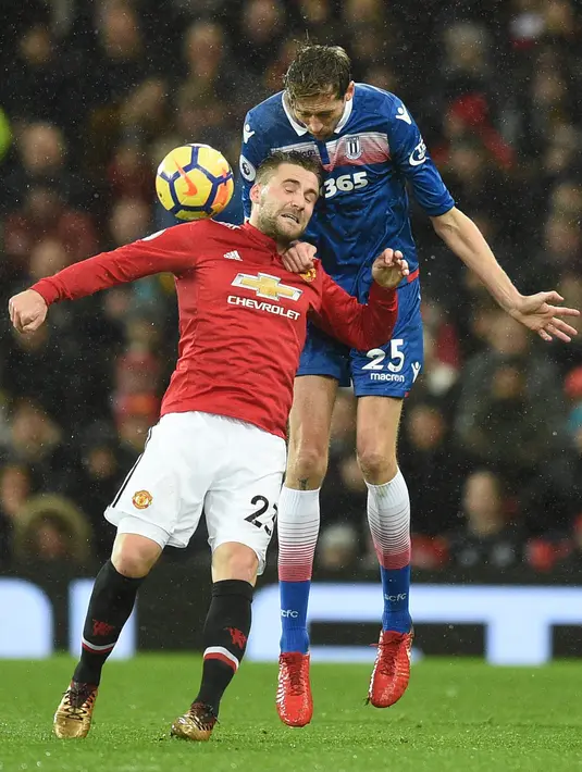 Striker Stoke City, Peter Crouch berebut bola dengan bek Manchester United, Luke Shaw pada laga pekan ke-23 Premier League 2017-2018 di Old Trafford, Senin (15/1). Manchester United mencetak tiga gol tanpa balas di kandnag sendiri. (Oli SCARFF/AFP)
