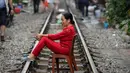 Seorang wanita Vietnam duduk di atas kursi di tengah jalur kereta api yang melintasi kawasan permukiman di Hanoi, 20 Oktober 2018. Rel kereta ini menjadi titik bagi wisatawan untuk berfoto dan mengunggahnya di jejaring sosial. (Nhac NGUYEN/AFP)