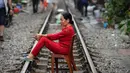 Seorang wanita Vietnam duduk di atas kursi di tengah jalur kereta api yang melintasi kawasan permukiman di Hanoi, 20 Oktober 2018. Rel kereta ini menjadi titik bagi wisatawan untuk berfoto dan mengunggahnya di jejaring sosial. (Nhac NGUYEN/AFP)