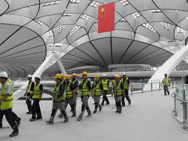 Para pekerja berjalan dalam Terminal Bandara Internasional Daxing Beijing, China, Selasa (9/7/2019). Bandara yang selesai pada 30 Juni 2019 tersebut dijadwalkan dibuka pada 30 September 2019. (GREG BAKER/AFP)