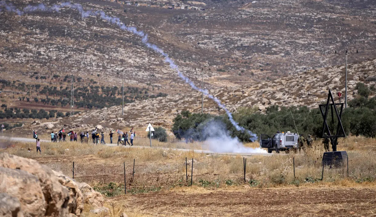 Tentara Israel menembakkan gas air mata untuk membubarkan pengunjuk rasa Palestina saat membakar ban dan memblokir jalan yang melewati Desa Mughayer, Tepi Barat, utara Ramallah, 29 Juli 2022. Warga Palestina yang memprotes aktivitas permukiman Israel memblokir jalan utama dan bentrok dengan pemukim Israel, sementara tentara menembakkan gas air mata untuk membubarkan mereka. (AP Photo/Nasser Nasser)