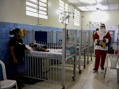 Seorang pria berpakaian seperti Sinterklas berjalan menyusuri lorong untuk mengantarkan hadiah kepada anak-anak yang dirawat di ruang gawat darurat sebuah rumah sakit di lingkungan El Cementerio di Caracas, Venezuela pada 25 Desember 2023. (Pedro Rances Mattey / AFP)