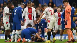 Para pemain Chelsea dan Southampton menghampiri bek Chelsea, Cesar Azpilicueta yang mengalami cedera akibat tendangan salto penyerang Southampton, Sekou Mara yang mengenai kepala selama pertandingan Liga Inggris di Stamford Bridge di London (18/2/2023). (AFP/Glyn Kirk)