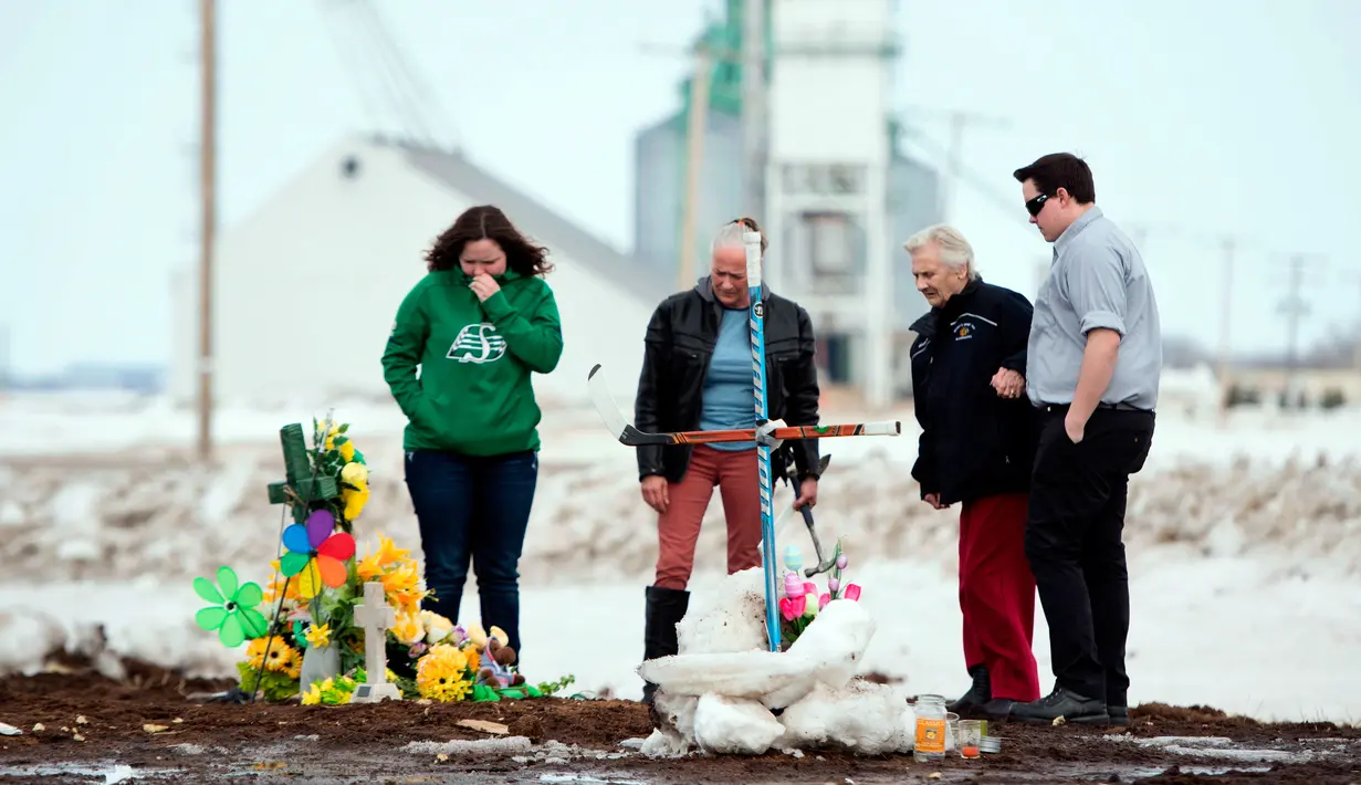Sebuah keluarga menempatkan salib yang terbuat dari tongkat hoki untuk memberi penghormatan kepada korban kecelakaan bus di Provinsi Saskatchewan, Kanada (9/4). (Jonathan Hayward/The Canadian Press via AP)