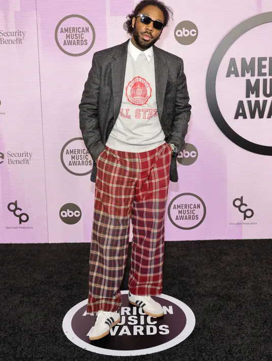 <p>Brent Faiyaz tampil sangat kasual dengan blazer abu-abu. Di bagian dalam, Brent mengenakan kemeja putih yang dilayer dengan sweater bermotif tulisan dan celana panjang merah garis-garis. Foto: Vogue.</p>