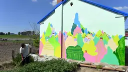 Seorang petani bekerja di samping sebuah rumah yang dihiasi lukisan di Desa Qingshui, Kota Changchun, China timur laut (18/6/2020). Para mahasiswa dan pengajar dari Universitas Seni Jilin menghiasi desa tersebut dengan mural. (Xinhua/Lin Hong)