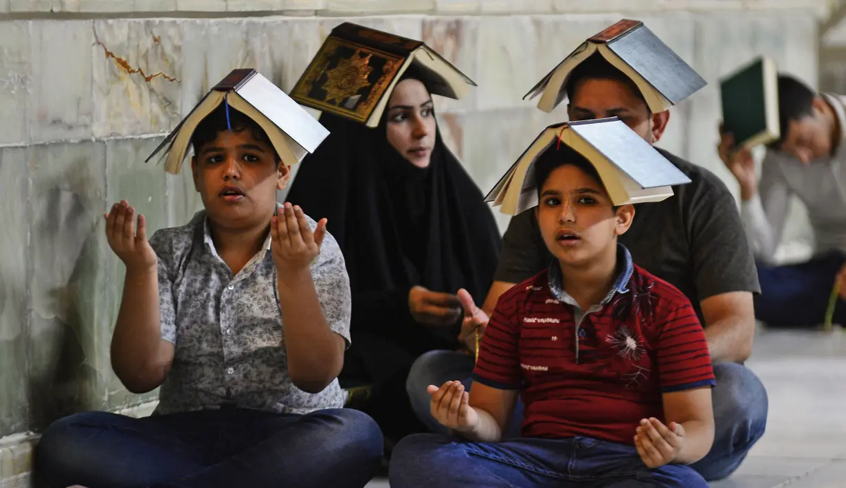 Para jemaah syiah manaruh kitab suci Al-Quran di atas kepala mereka saat menyambut malam lailatul qadar di Makam Suci Imam Ali, Najaf, Irak, Sabtu (16/5/2020). Ritual saat berdoa dan meminta hajat kepada Tuhan ini sudah berlangsung selama berabad-abad lamanya. (HAIDAR HAMDANI/AFP)