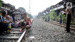 Aktivitas warga berjemur di bantaran rel di kawasan pemukiman padat Pejompongan, Jakarta, Selasa (6/7/2021). Berjemur diri di bawah matahari di antara pukul 08.00-11.00 WIB merupakan salah satu upaya paling sederhana untuk menjaga kesehatan selama wabah virus COVID-19. (Liputan6.com/Faizal Fanani)