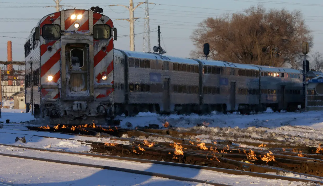 Sebuah kereta komuter melaju menuju pusat kota Chicago ketika api menyala di sepanjang rel di dekat stasiun Metra Western Avenue, 29 Januari 2019. Metra memakai sistem pemanas berbahan bakar gas untuk menghangatkan lintasan yang dingin. (AP/Kiichiro Sato)