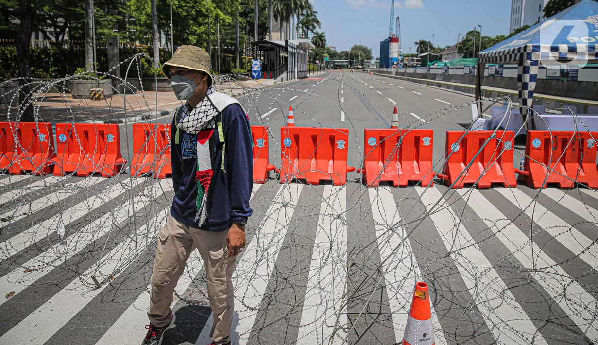 Seorang pria berjalan dekat kawat berduri di kawasan Jalan MH Thamrin, Jakarta, Kamis (2/12/2021). Polda Metro Jaya memasang barikade di sejumlah titik menuju kawasan Patung Kuda-Monumen Nasional (Monas) Jakarta Pusat guna mengantisipasi kerumunan massa aksi Reuni 212. (Liputan6.com/Faizal Fanani)