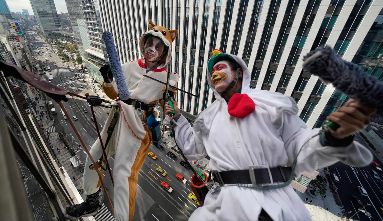 Pembersih jendela wanita berkostum ayam jago dan anjing membersihkan jendela gedung di kawasan perbelanjaan dan bisnis Tokyo, Jepang (20/12). (AP Photo / Shizuo Kambayashi)