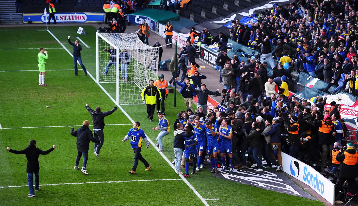 Fans AFC Wimbledon turun ke lapangan saat merayakan gol Jack Midson ke gawang Milton Keynes Dons pada laga FA Cup (2/12/2012). Pada Era 80-an Wimbledon jadi klub yang dibenci karena permainan agresif yang kasar sehingga membuat pemain lawan ketar-ketir di lapangan. (AFP/Adrian Dennis)