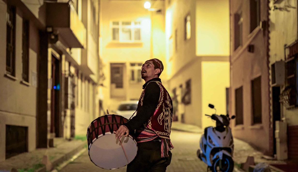 Para penabuh drum berkeliling membawa genderang sambil mengenakan pakaian tradisional seperti fez dan rompi. Tampak dalam foto, seorang pemain drum Turki memainkan drum dan menyanyikan lagu-lagu tradisional di jalanan Istanbul, untuk membangunkan umat Muslim untuk sahur, yaitu makan malam Ramadan, pada 24 Februari 2026. (Yasin AKGUL/AFP)