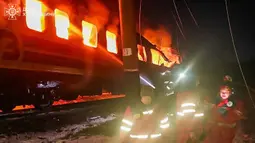 Menurut keterangan otoritas Ukraina, serangan ini menewaskan sedikitnya empat orang dan melukai dua lainnya. Tampak dalam foto yang diberikan dan dirilis oleh Layanan Darurat Ukraina pada 27 Januari 2026 ini, petugas medis Ukraina berdiri di samping gerbong kereta yang terbakar setelah serangan udara di lokasi yang tidak diungkapkan di wilayah Kharkiv, di tengah invasi Rusia ke Ukraina. (Handout/UKRAINIAN EMERGENCY SERVICE/AFP)