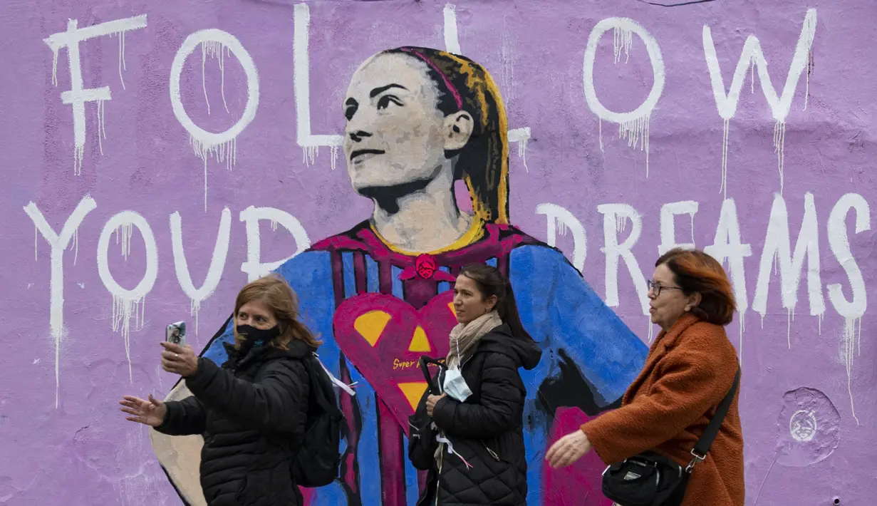 Sejumlah pejalan kaki melintasi mural bergambar Alexia Putellas yang dibuat oleh seniman Italia, TvBoy di Barcelona, 20 Maret 2022. (AFP/Josep Lago)