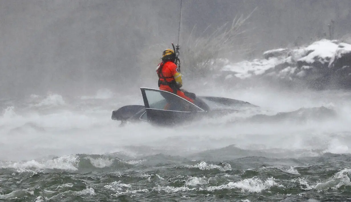 Penyelam Penjaga Pantai AS diturunkan dari helikopter untuk menarik tubuh pengendara mobil yang terjebak dalam arus deras di tepi Air Terjun Niagara, New York, AS, 8 Desember 2021. Mobil sedan hitam itu hampir tenggelam seluruhnya. (Derek Gee/The Buffalo News via AP)