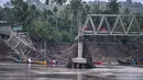 Sisa rangka jembatan terlihat menggantung di atas aliran sungai Peusangan yang masih deras. Tampak dalam foto, perahu-perahu yang digunakan untuk mengangkut penumpang menyeberangi Sungai Peusangan terlihat melewati jembatan yang runtuh di Kuta Blang, Kabupaten Bireuen, Provinsi Aceh, Selasa 9 Desember 2025. (CHAIDEER MAHYUDDIN/AFP)