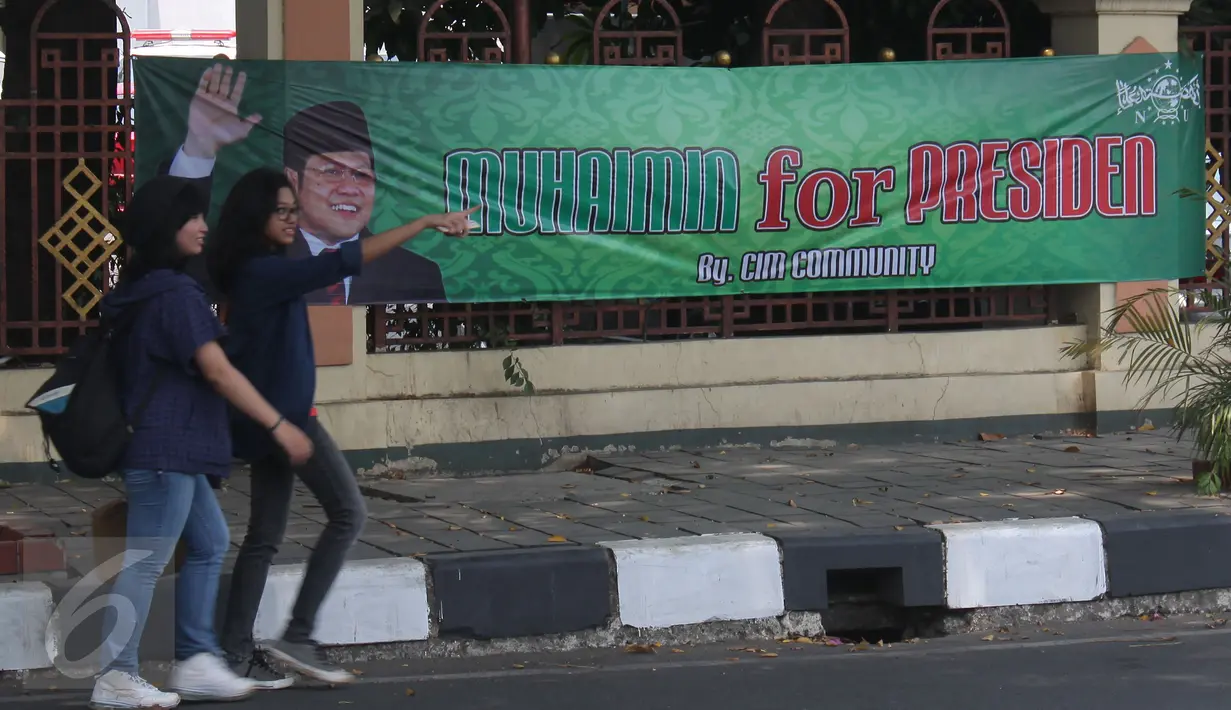 Dua remaja berjalan melintasi spanduk  'Muhaimin for President' di pagar Masjid Sunda Kelapa, Jakarta, Sabtu (12/9). Pemasangan spanduk itu melanggar UU tentang larangan penggunaan tempat ibadah sebagai tempat kampanye. (Liputan6.com/Angga Yuniar)
