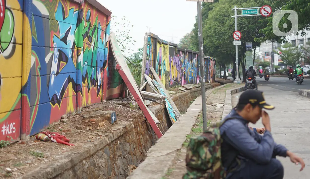 Seorang pria duduk di dekat tembok Jalan Juanda yang ambruk di kawasan Depok, Jawa Barat, Senin (2/12/2019). Kondisi tembok yang dipenuhi mural tersebut mulai rapuh dan sebagian sisinya telah ambruk serta miring sehingga membahayakan pejalan kaki. (Liputan6.com/Immanuel Antonius)