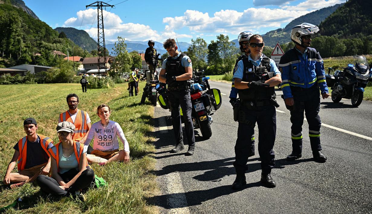 Polisi Prancis (kanan) berdiri di samping pengunjuk rasa lingkungan setelah aksi protes mereka menghentikan sementara balapan pada etape ke-10 Tour de France, antara Morzine dan Megeve, di Pegunungan Alpen Prancis, pada 12 Juli 2022. (AFP/Marco Bertorello)