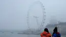 Wisatawan mengambil gambar The London Eye saat diselimuti kabut Inggris, Senin, (23/1). Aktifitas warga menjadi terganggu karena terbatasnya jarak pandang (AP Photo / Alastair Grant)