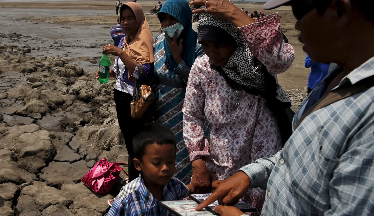 Warga menjajakan kaset video lumpur kepada wisatawan yang mengunjungi lumpur Lapindo di Sidoarjo, Jawa Timur, 11 Oktober 2015. Beberapa tahun silam, Porong didera bencana, namun kini kawasan tersebut menjadi objek wisata tak biasa. (REUTERS/Beawiharta)