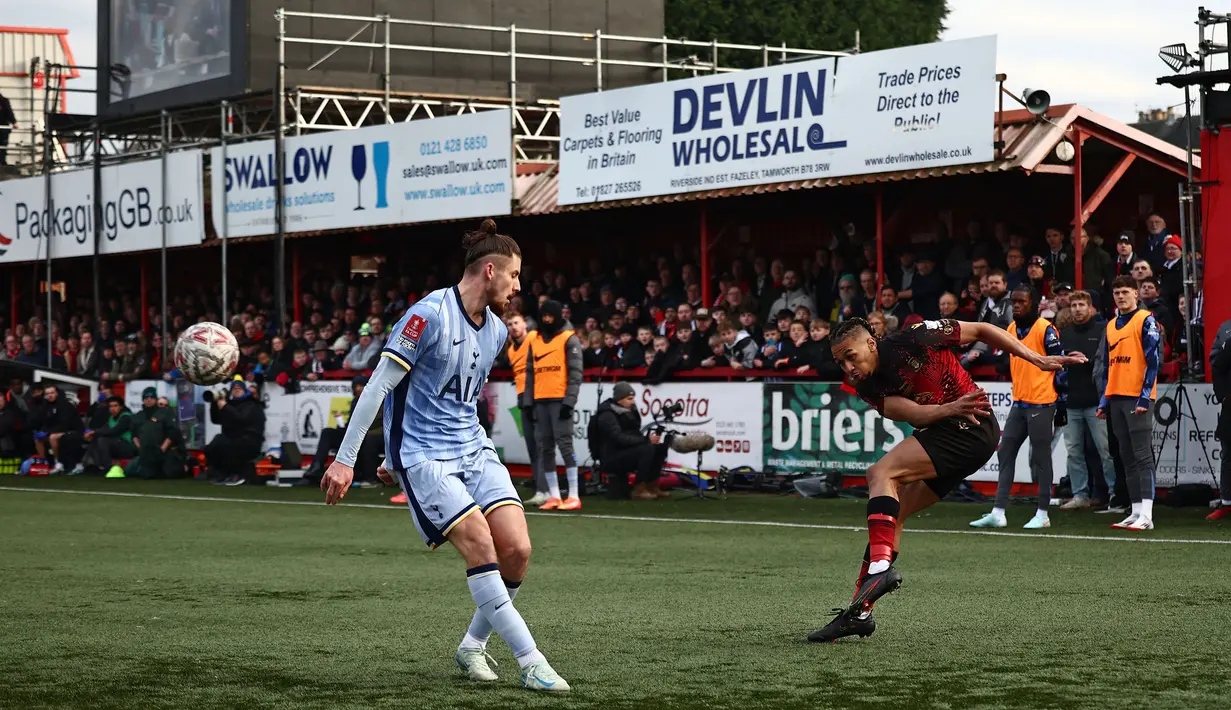 Pemain Tamworth, Kai Williams (kanan) melakukan umpan silang dibayangi pemain Tottenham Hotspur pada laga Piala FA 2024/2025 di The Lamb Ground, Tamworth, Inggris, Minggu (12/01/2025) waktu setempat. (AFP/Henry Nicholls)