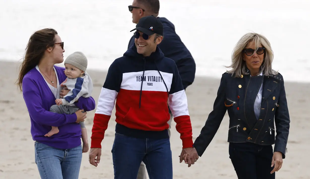 <p>Presiden Prancis Emmanuel Macron dan istrinya Brigitte Macron berbincang dengan seorang wanita yang menggendong anaknya saat mereka berjalan di sepanjang pantai di Le Touquet, Sabtu (23/4/2022). Emmanuel Macron akan menghadapi Marine Le Pen dalam putaran kedua pemilihan presiden (pilpres) pada 24 April 2022. (Ludovic MARIN / AFP)</p>
