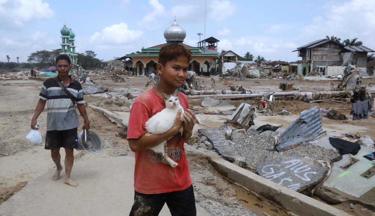 Akses jalan hingga tumpukan material banjir masih menyulitkan relawan untuk segera melakukan evakuasi korban. Tampak dalam foto, seorang penyintas menggendong kucing sambil berjalan di area yang terdampak banjir bandang di Aceh Tamiang, Pulau Sumatra, Jumat 5 Desember 2025. (AP Photo/Binsar Bakkara)
