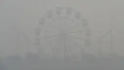 Permainan kincir terlihat di tengah kondisi asap tebal di Lahore, Pakistan (21/11/2019). Akibat kabut asap tebal penduduk Lahore mengeluh sakit tenggorokan, mata gatal dan penyakit lainnya.  (AFP Photo/Arif Ali)