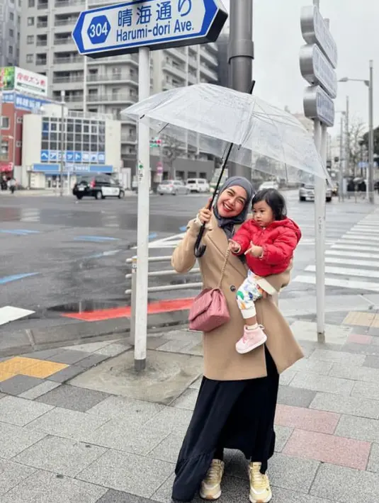 Ria Ricis tampil mengenakan blazer coat coklat dipadukan rok panjang hitam dan kerudung abu-abunya. Moana mengenakan padding jaket merah. [@riaricis1795]