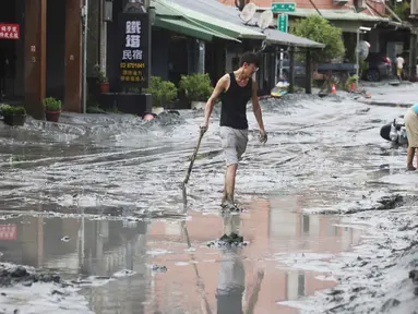 Seorang warga berjalan dengan sekop di sepanjang jalan yang tertutup lumpur di Hualien pada 24 September 2025, setelah bendungan danau jebol akibat terjangan Topan Super Ragasa. (I-Hwa Cheng/AFP)
