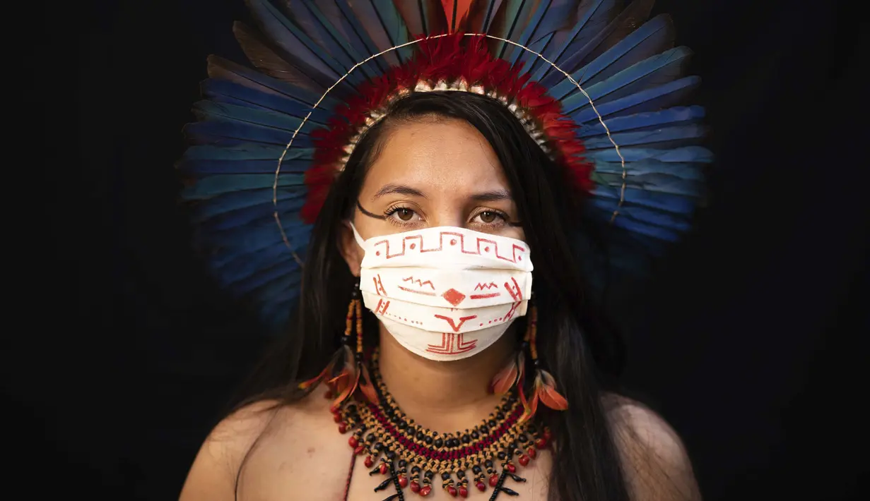 Samela (23) dari kelompok etnis pribumi Sateré Mawé mengenakan pakaian tradisional sukunya dan masker saat pandemi virus corona COVID-19 di Manaus, Brasil, Rabu (27/5/2020). Ibu Samela, Sonia Vilacio pulih dari gejala mirip COVID-19 menggunakan obat alami di rumah. (AP Photo/Felipe Dana)