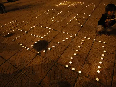 Seorang anak kecil tampak menyalakan lilin di samping pesan ajakan untuk mendoakan para korban Malaysia Airlines MH 370 (REUTERS / Edgar Su)