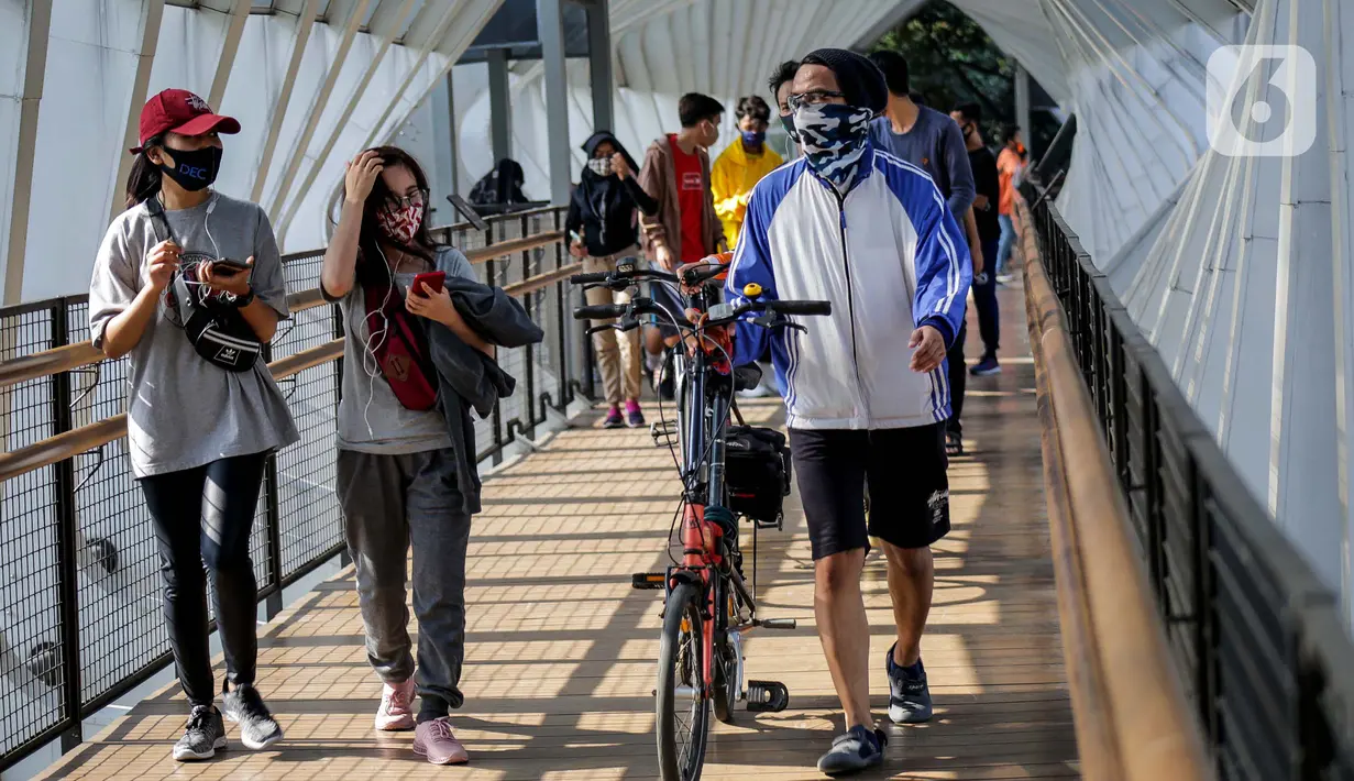 Warga melewati jembatan penyeberangan orang saat berolahraga menggunakan sepeda di sepanjang Jalan Sudirman, Jakarta, Minggu (26/7/2020). Perluasan jalur sepeda sementara dilakukan sebagai dampak peniadaan hari bebas kendaraan bermotor (HBKB) di Jalan Sudirman-Thamrin. (Liputan6.com/Faizal Fanani)
