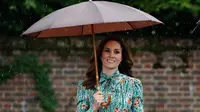 Duchess  of Cambridge, Kate Middleton berjalan dibawah payung cokelatnya di taman Istana Kensington, London, Rabu (30/8). Kate terlihat anggun dalam balutan gaun hijau dengan bunga Poppy merah sebagai hiasannya. (Kirsty Wigglesworth/AP)