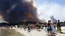 Sejumlah wisatawan dievakuasi dari pantai Le Lavandou, Prancis Selatan, akibat kebakaran hutan yang semakin meluas, Rabu (26/7). Sekitar 10.000 orang terpaksa meninggalkan hunian, dievakuasi ke tempat yang lebih aman. (AP/Claude Paris)