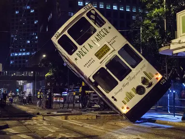Sebuah trem double-decker diangkat menggunakan crane setelah terbalik di jalan utama di Hong Kong, Kamis (6/4). Kecelakaan yang terjadi tengah malam waktu setempat itu mengakibatkan 11 orang mengalami luka-luka. (ANTHONY WALLACE / AFP)