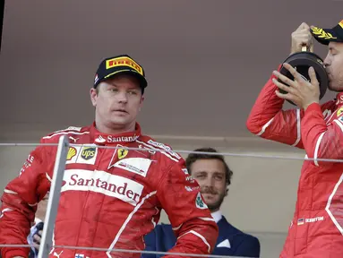 Pebalap Ferrari, Sebastian Vettel merayakan kemenangan sementara Kimi Raikkonen hanya melihatnya dengan tatapan kosong pada F1 GP Monako, (28/5/2017). (AP/Claude Paris)