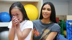 Kim Kardashian berpose dengan seorang anak  penyandang cacat di Rashid Media Centre, Dubai (16/1). Kim Kardashian diberi kesempatan untuk melihat karya seni yang dibuat oleh anak-anak penyandang cacat. (AFP Photo And Rashid Media Center/Stringer)