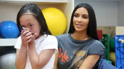 Kim Kardashian berpose dengan seorang anak  penyandang cacat di Rashid Media Centre, Dubai (16/1). Kim Kardashian diberi kesempatan untuk melihat karya seni yang dibuat oleh anak-anak penyandang cacat. (AFP Photo And Rashid Media Center/Stringer)