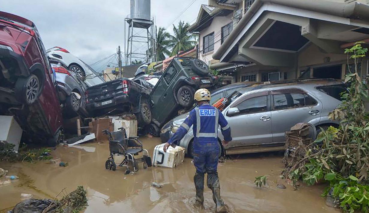 Seorang petugas penyelamat berjalan melewati tumpukan mobil yang hanyut oleh banjir pada puncak Topan Kalmaegi di sebuah permukiman di Kota Cebu, Filipina tengah, pada Selasa 4 November 2025. Sekretaris Jenderal Palang Merah Filipina, Gwendolyn Pang, mengatakan banyak warga terjebak di atap rumah akibat banjir. (Alan TANGCAWAN/AFP)
