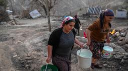 Dua orang wanita membawa ember berisi air di kawasan desa Yaylakonak distrik Adiyaman, Turki, Minggu (19/2/2023). Gempa bumi berkekuatan 7,8 magnitudo melanda dekat Gaziantep, Turki, pada dini hari tanggal 6 Februari, diikuti oleh gempa susulan berkekuatan 7,5 magnitudo setelah tengah hari. Gempa bumi tersebut menyebabkan kehancuran yang meluas di Turki Selatan dan Suriah Utara dan telah menewaskan lebih dari 40.000 orang. (BULENT KILIC/AFP)