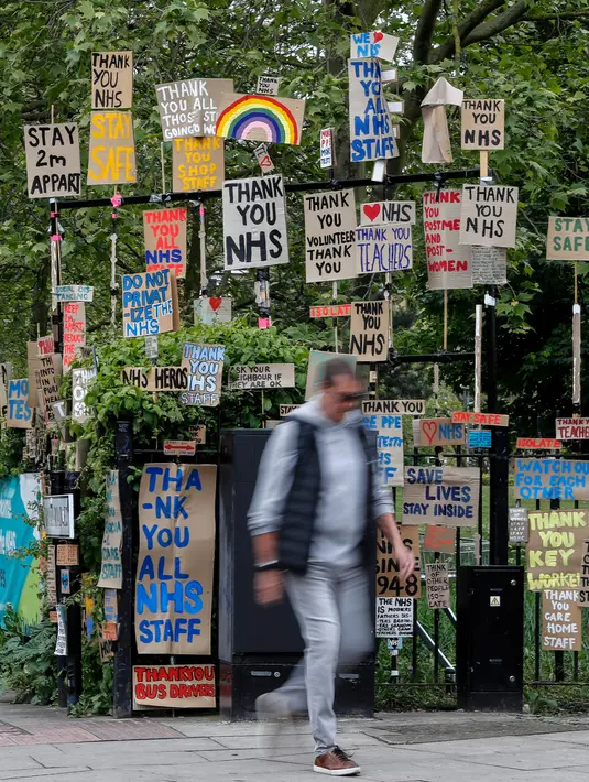 Seorang pria berjalan melewati kumpulan plakat yang dirancang oleh seniman lokal Peter Liversidge untuk mendukung Layanan Kesehatan Nasional (National Health Service/NHS) di London, Inggris, (29/4/2020). (Xinhua/Han Yan)