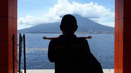 Siluet Direktur Teknis Malut United, Yeyen Tumena, saat mengambil foto salah satu staf klub dengan latar belakang gunung ketika tiba di pelabuhan Tidore, Maluku Utara. (Bola.com/Okie Prabhowo)