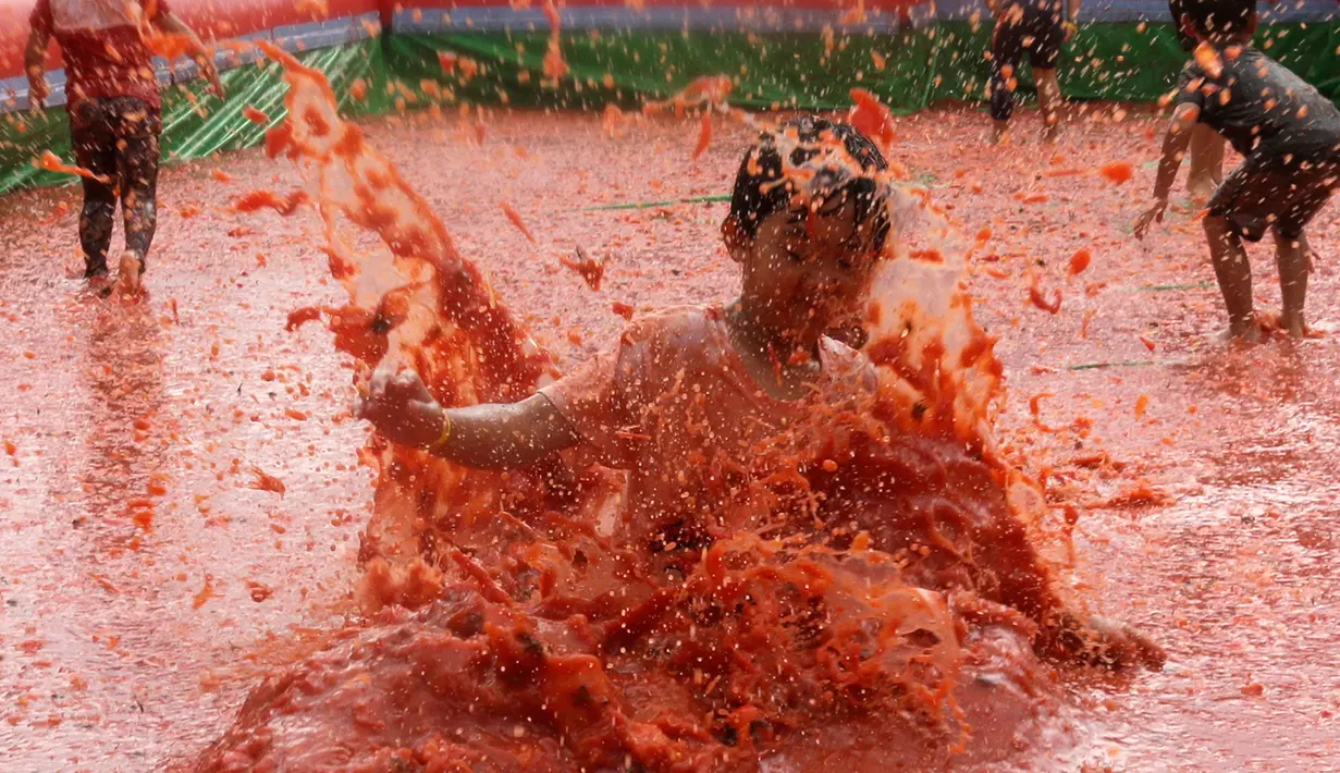 Seorang anak melompat ke dalam kolam berisi tomat selama Festival Tomat di Hwacheon, Korea Selatan, 5 Agustus 2017. Di festival ini, pengunjung bebas memetik tomat yang siap dipanen, membuat saus tomat, dan mandi tomat. (AP Photo/Ahn Young-joon)