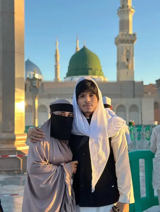 Atta Halilintar berpose bersama sang istri Aurelie Hermansyah. Atta tampak mengenakan outfit berwarna hitam-putih dengan syal yang dikenakannya di kepala, sedangkan Aurelie tampil dengan outfit berwarna cokelat, masih lengkap dengan burqa berwarna hitam. Foto: Instagram.