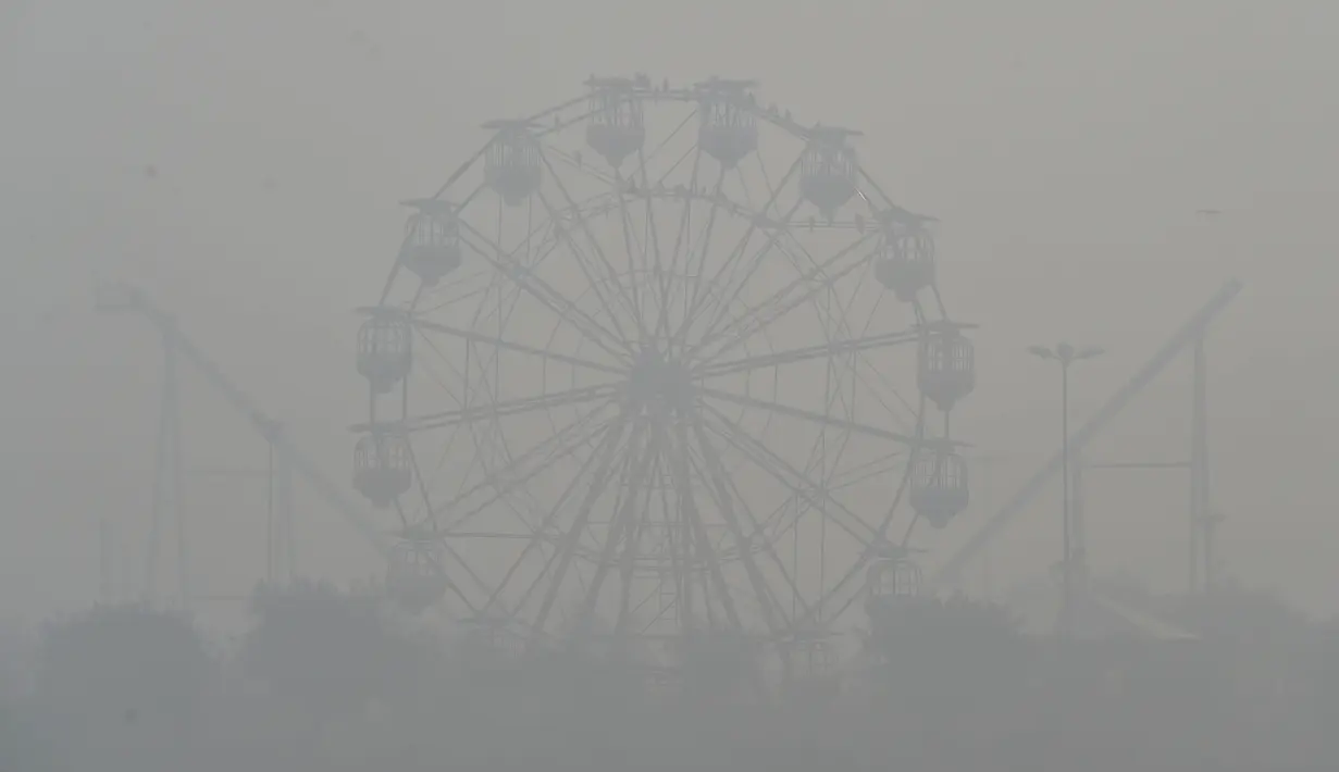 Permainan kincir terlihat di tengah kondisi asap tebal di Lahore, Pakistan (21/11/2019). Akibat kabut asap tebal penduduk Lahore mengeluh sakit tenggorokan, mata gatal dan penyakit lainnya.  (AFP Photo/Arif Ali)